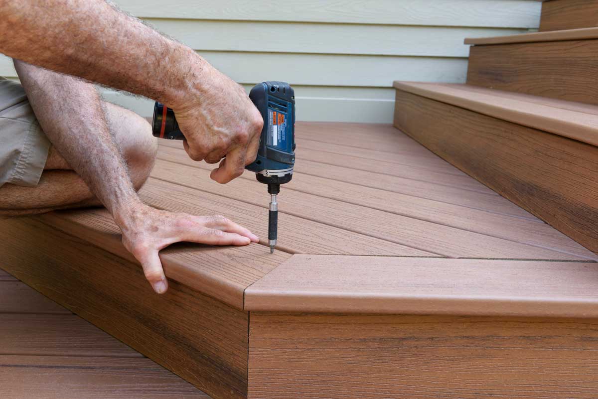 A man's hands drilling a plank to a wooden deck