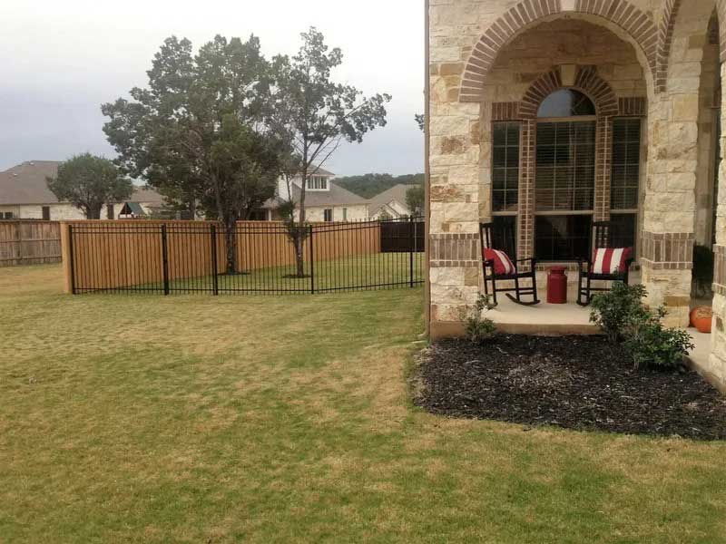 A black iron fence marking a backyard on a flat, grassy field enxt to a large house
